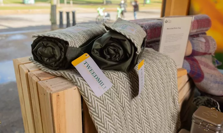 A green picnic rug is rolled up in the foreground. Pink blankets are folded in the background. 